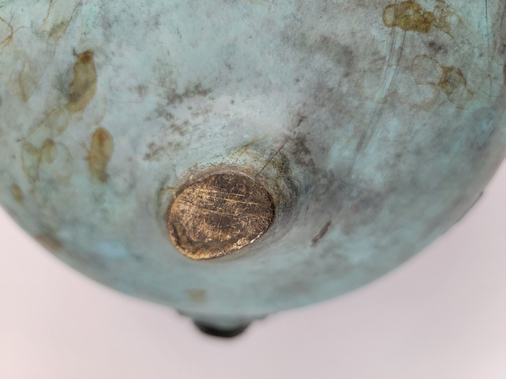 A tripod Chinese bronze censer decorated with raised dragon motifs, mask handles, and a verdigris surface finish. View XV