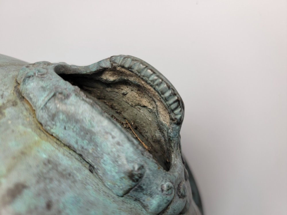 A tripod Chinese bronze censer decorated with raised dragon motifs, mask handles, and a verdigris surface finish. View XVII