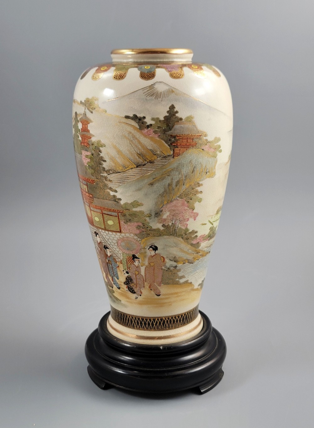 An antique Japanese Satsuma earthenware vase decorated with hand-painted landscape scenes, figures, and pagodas over a fine crackle glaze, sitting on a turned dark wood stand. View II