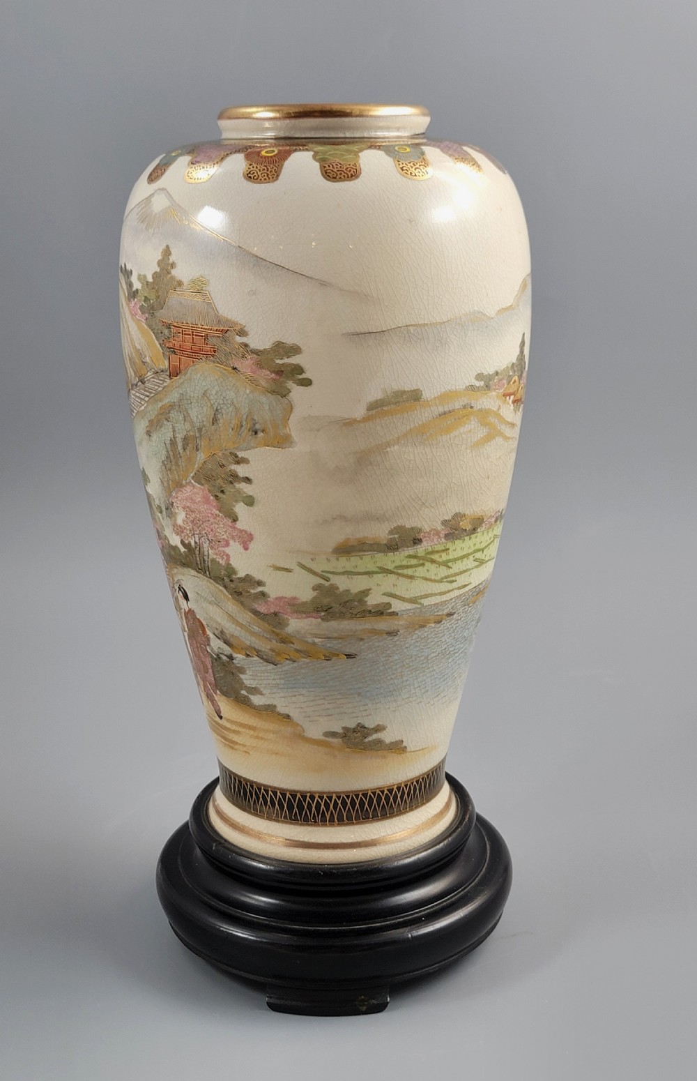 An antique Japanese Satsuma earthenware vase decorated with hand-painted landscape scenes, figures, and pagodas over a fine crackle glaze, sitting on a turned dark wood stand. View III