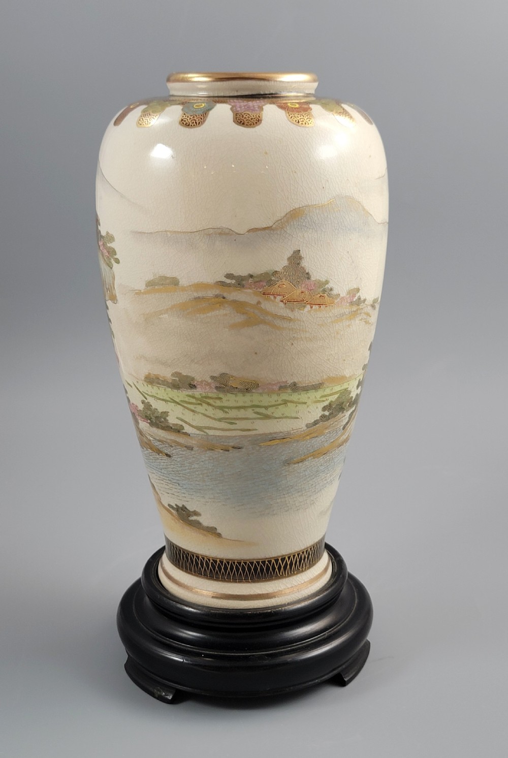 An antique Japanese Satsuma earthenware vase decorated with hand-painted landscape scenes, figures, and pagodas over a fine crackle glaze, sitting on a turned dark wood stand. View IV