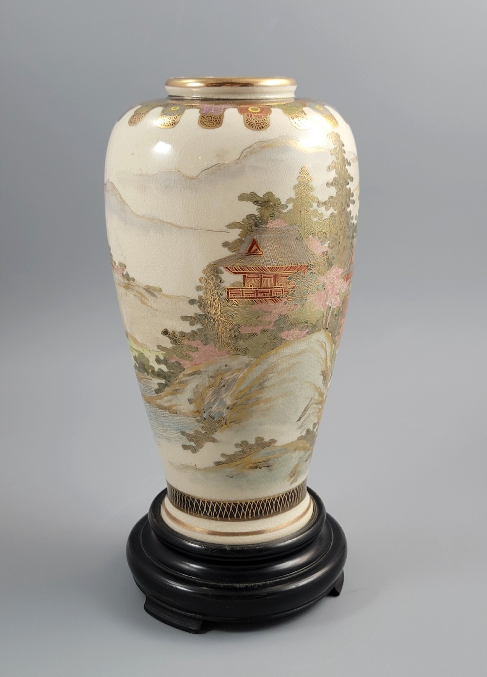 An antique Japanese Satsuma earthenware vase decorated with hand-painted landscape scenes, figures, and pagodas over a fine crackle glaze, sitting on a turned dark wood stand. View VI