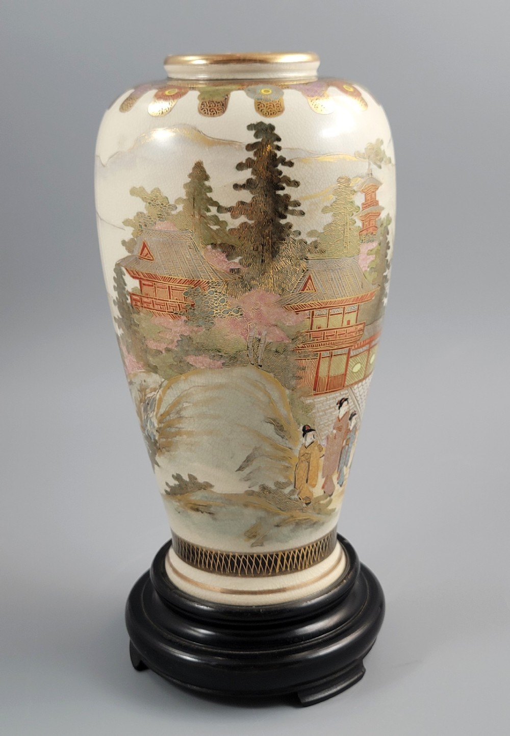 An antique Japanese Satsuma earthenware vase decorated with hand-painted landscape scenes, figures, and pagodas over a fine crackle glaze, sitting on a turned dark wood stand. View VII
