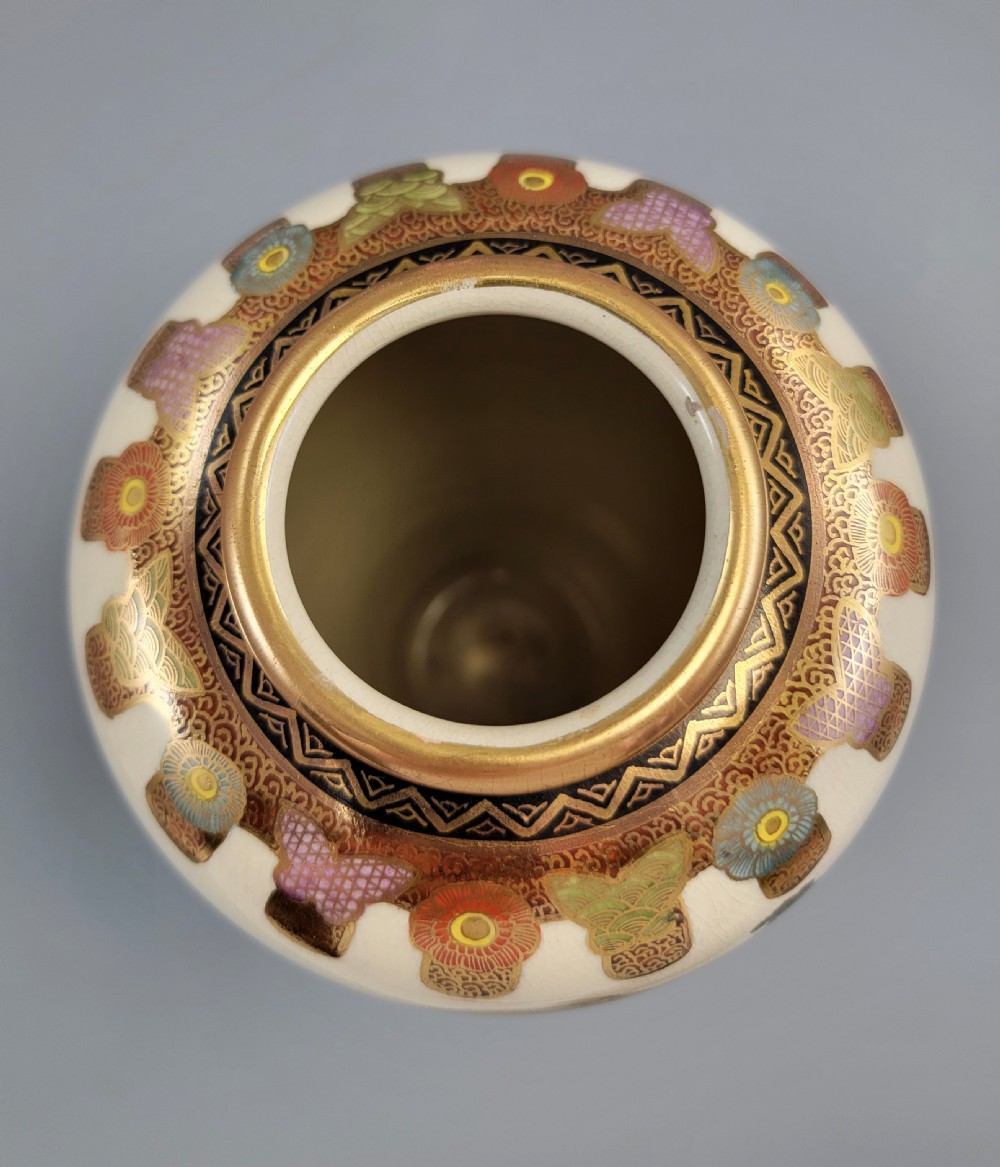 An antique Japanese Satsuma earthenware vase decorated with hand-painted landscape scenes, figures, and pagodas over a fine crackle glaze, sitting on a turned dark wood stand. View VIII