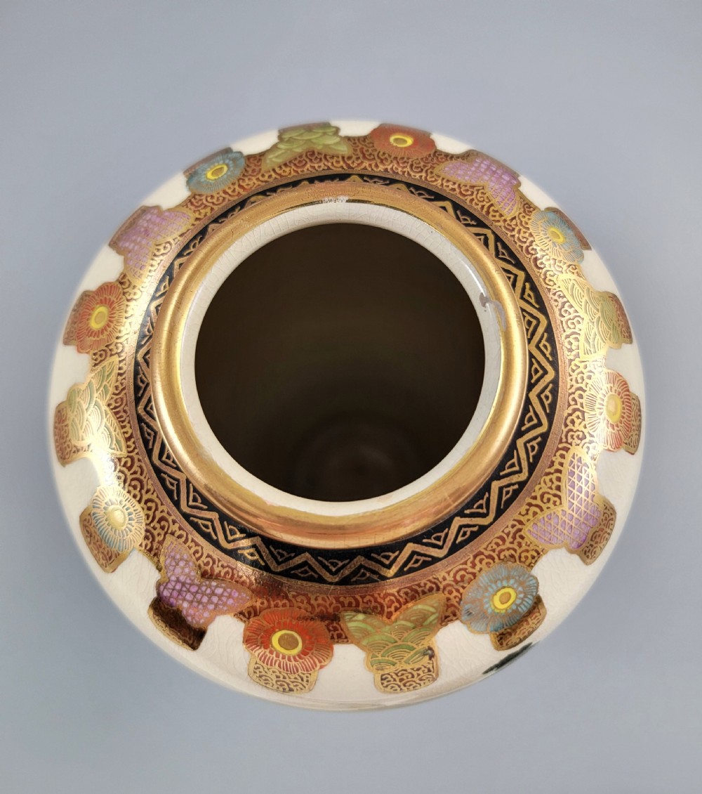 An antique Japanese Satsuma earthenware vase decorated with hand-painted landscape scenes, figures, and pagodas over a fine crackle glaze, sitting on a turned dark wood stand. View IX