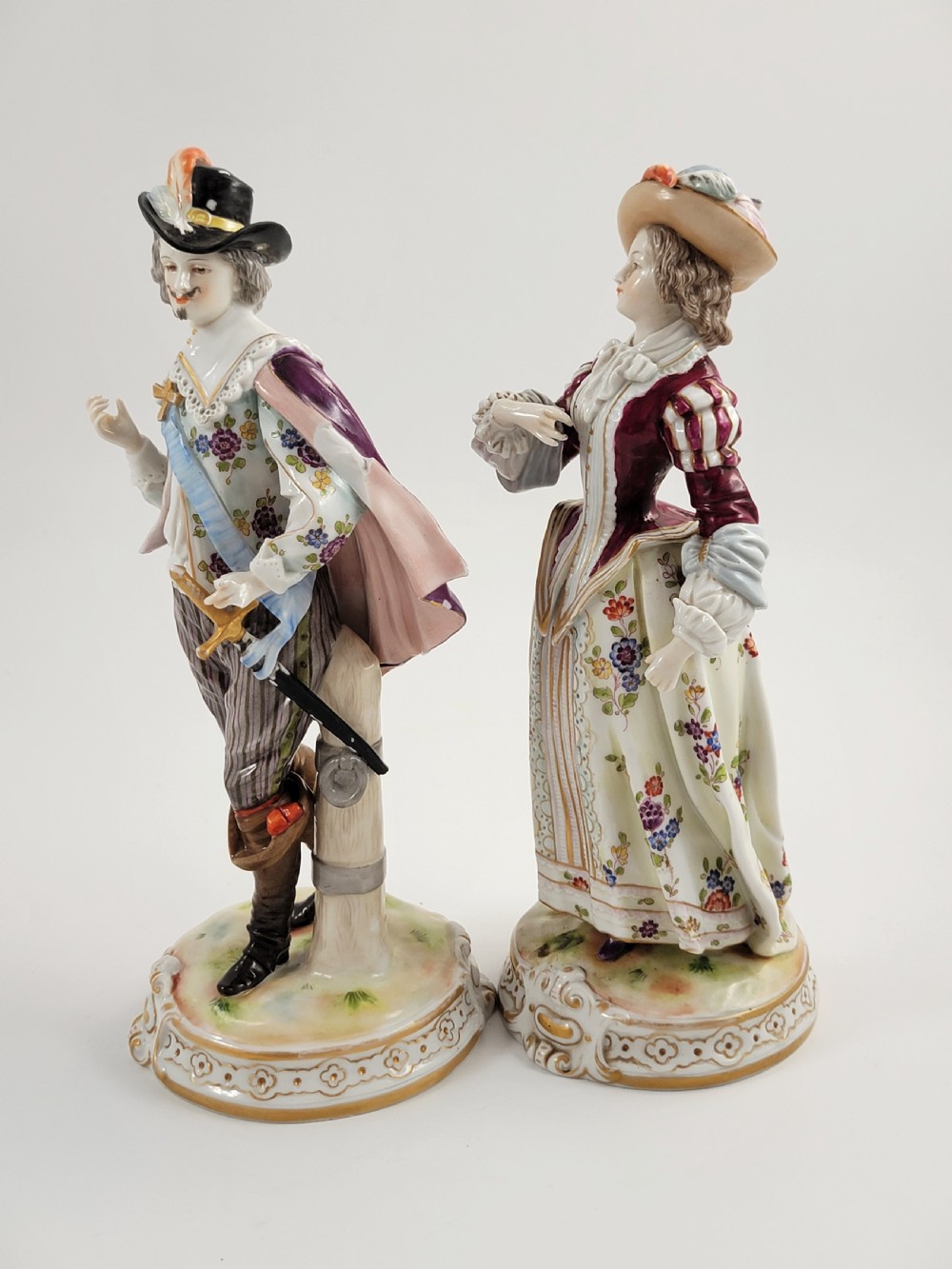 A pair of 18th-century hand-painted Ludwigsburg porcelain figures depicting a musketeer and a lady in detailed period attire standing on gilded Rococo scrollwork bases. View II