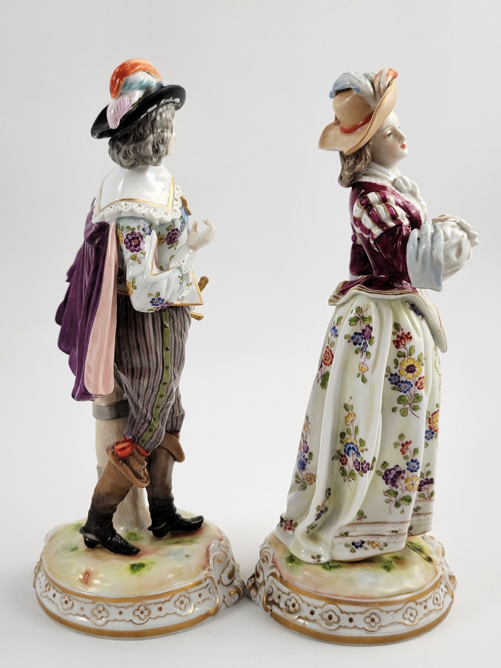 A pair of 18th-century hand-painted Ludwigsburg porcelain figures depicting a musketeer and a lady in detailed period attire standing on gilded Rococo scrollwork bases. View IV