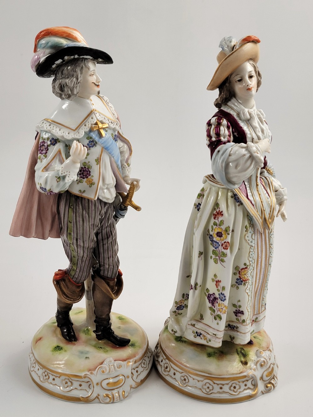 A pair of 18th-century hand-painted Ludwigsburg porcelain figures depicting a musketeer and a lady in detailed period attire standing on gilded Rococo scrollwork bases. View V