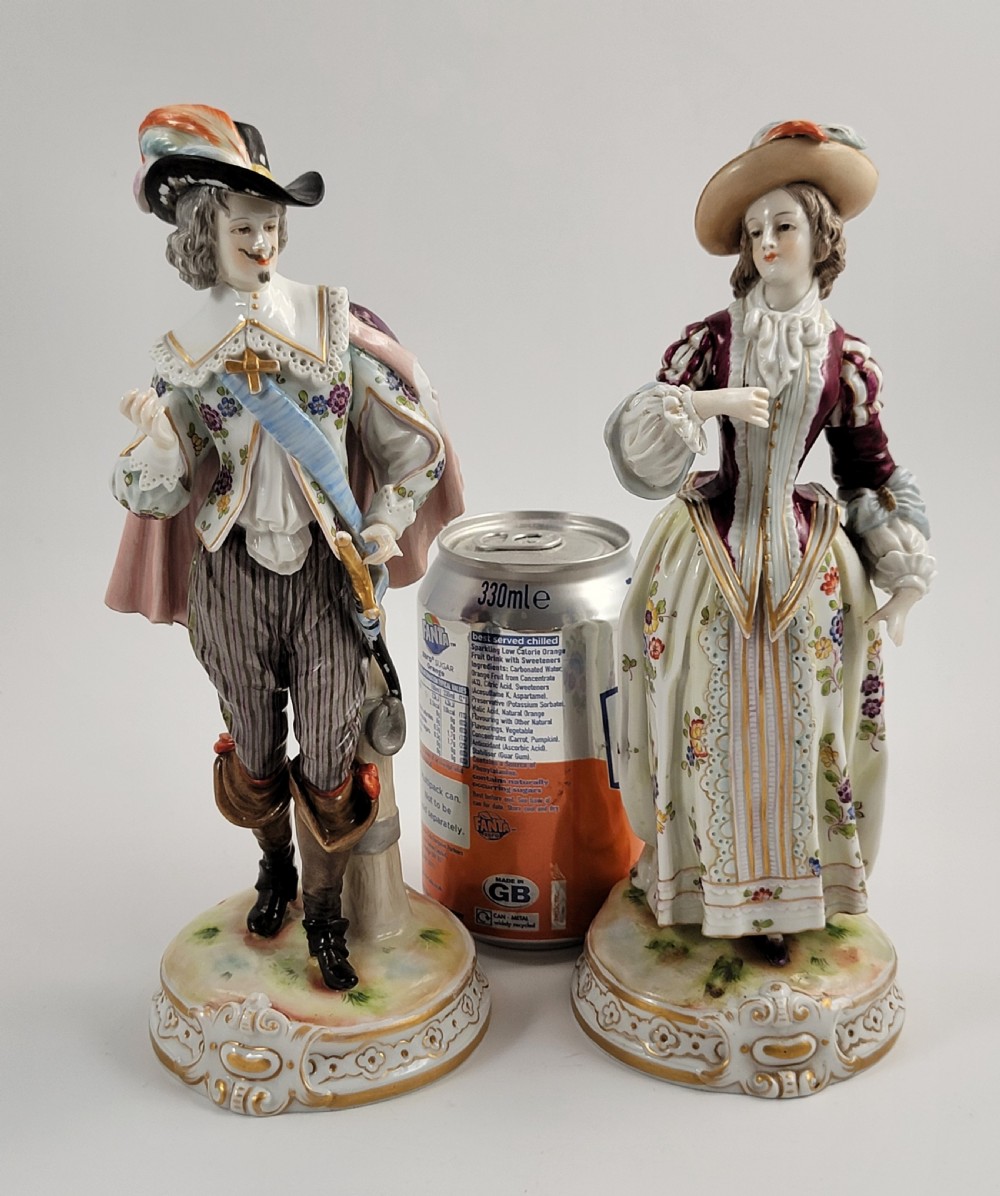 A pair of 18th-century hand-painted Ludwigsburg porcelain figures depicting a musketeer and a lady in detailed period attire standing on gilded Rococo scrollwork bases. View VII