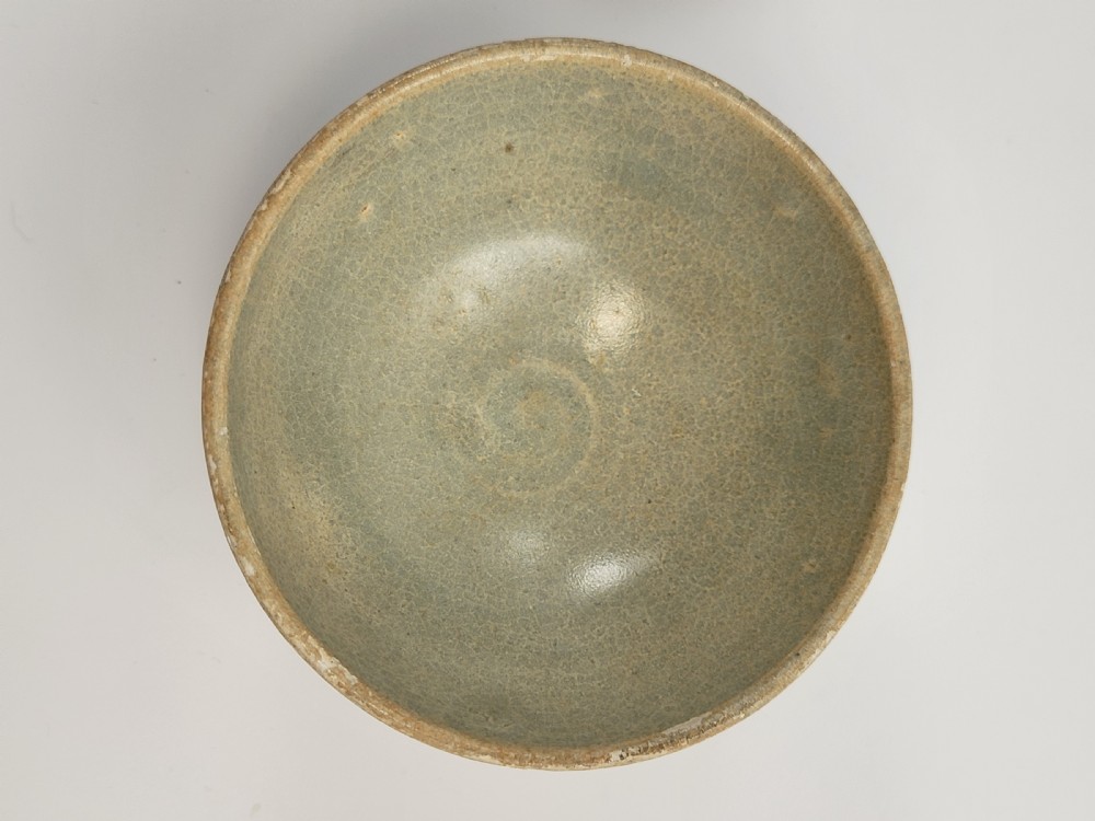A pale green celadon ceramic bowl with carved exterior lotus petal fluting displayed on a dark carved wooden stand. View VII