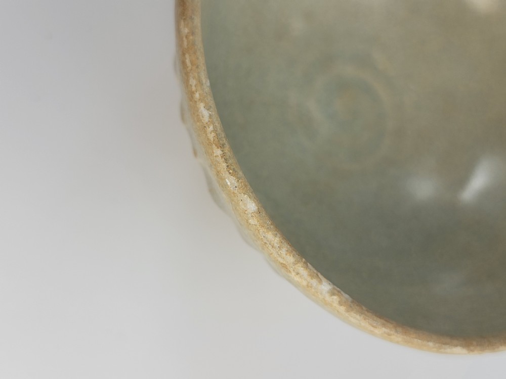 A pale green celadon ceramic bowl with carved exterior lotus petal fluting displayed on a dark carved wooden stand. View IX
