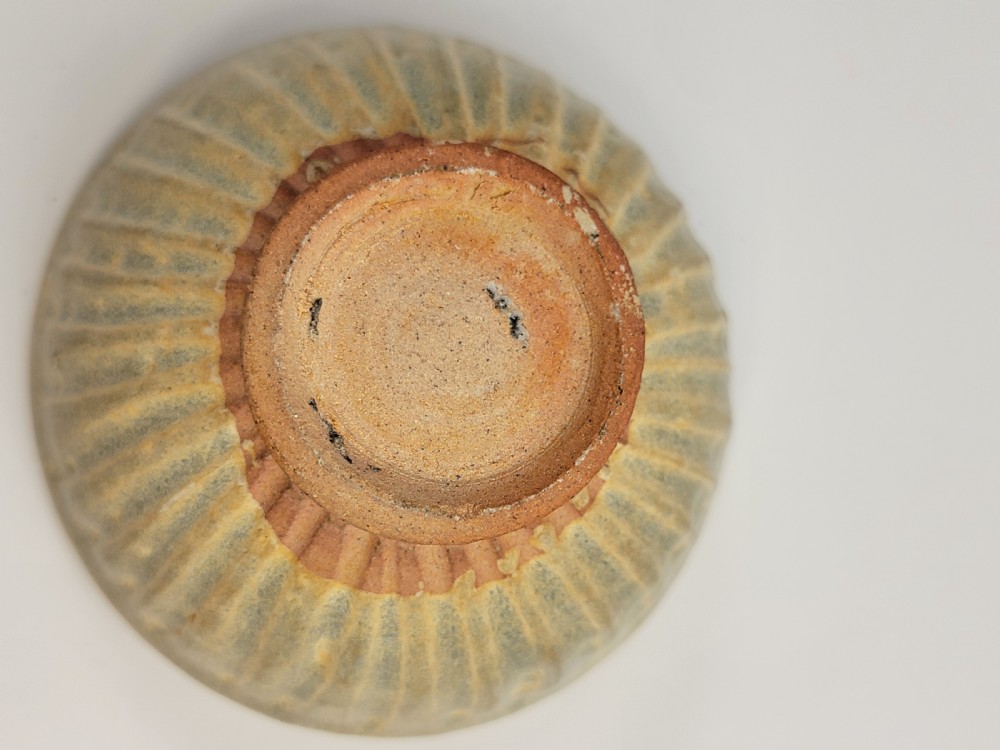 A pale green celadon ceramic bowl with carved exterior lotus petal fluting displayed on a dark carved wooden stand. View X