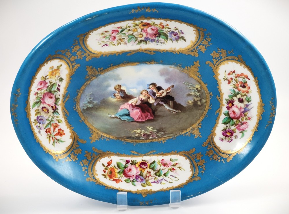 An oval French porcelain tray featuring a bleu celeste ground with hand-painted floral reserves and a central scene depicting figures in a landscape enclosed by gilt ornamentation.