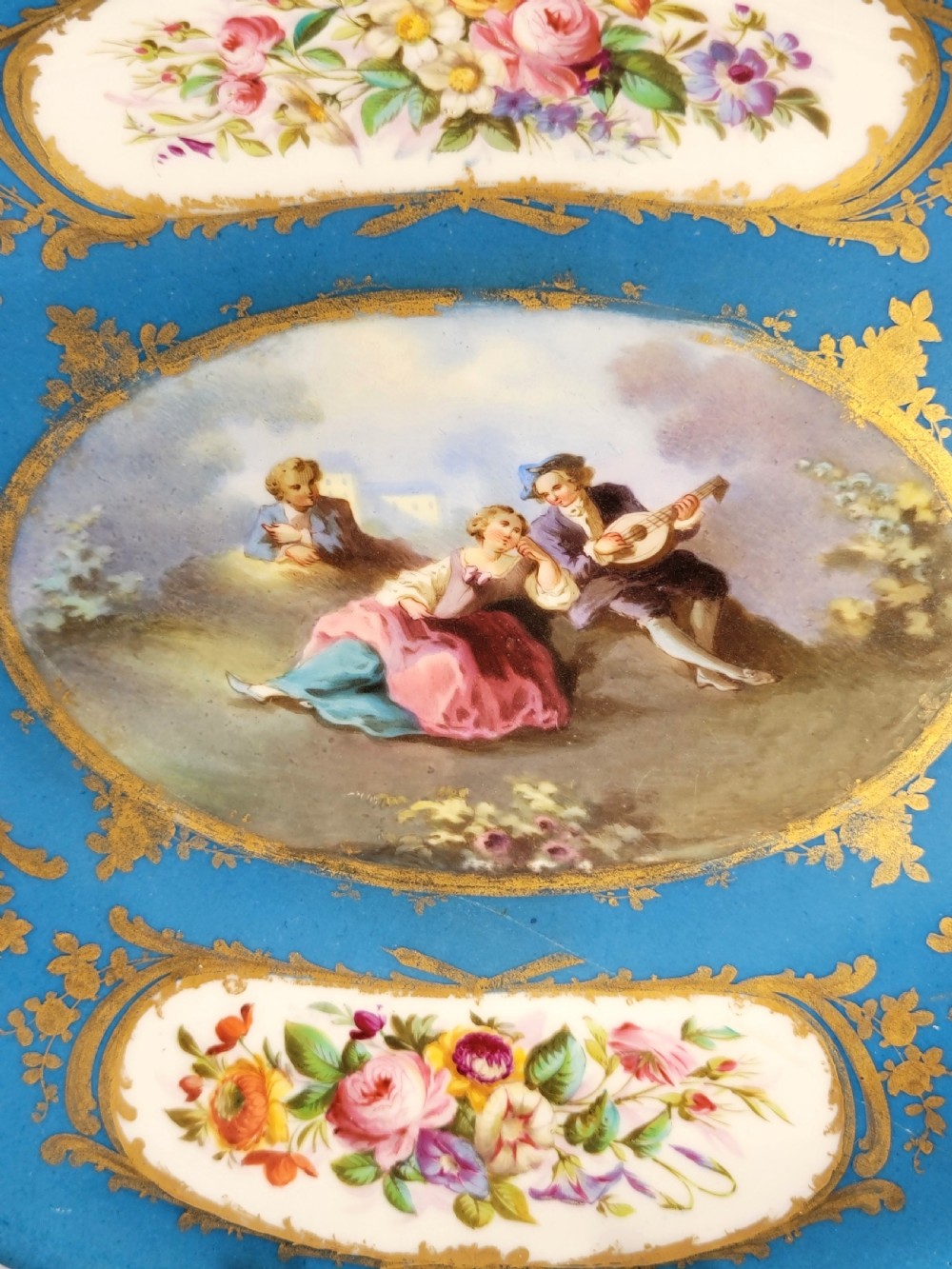 An oval French porcelain tray featuring a bleu celeste ground with hand-painted floral reserves and a central scene depicting figures in a landscape enclosed by gilt ornamentation. View III