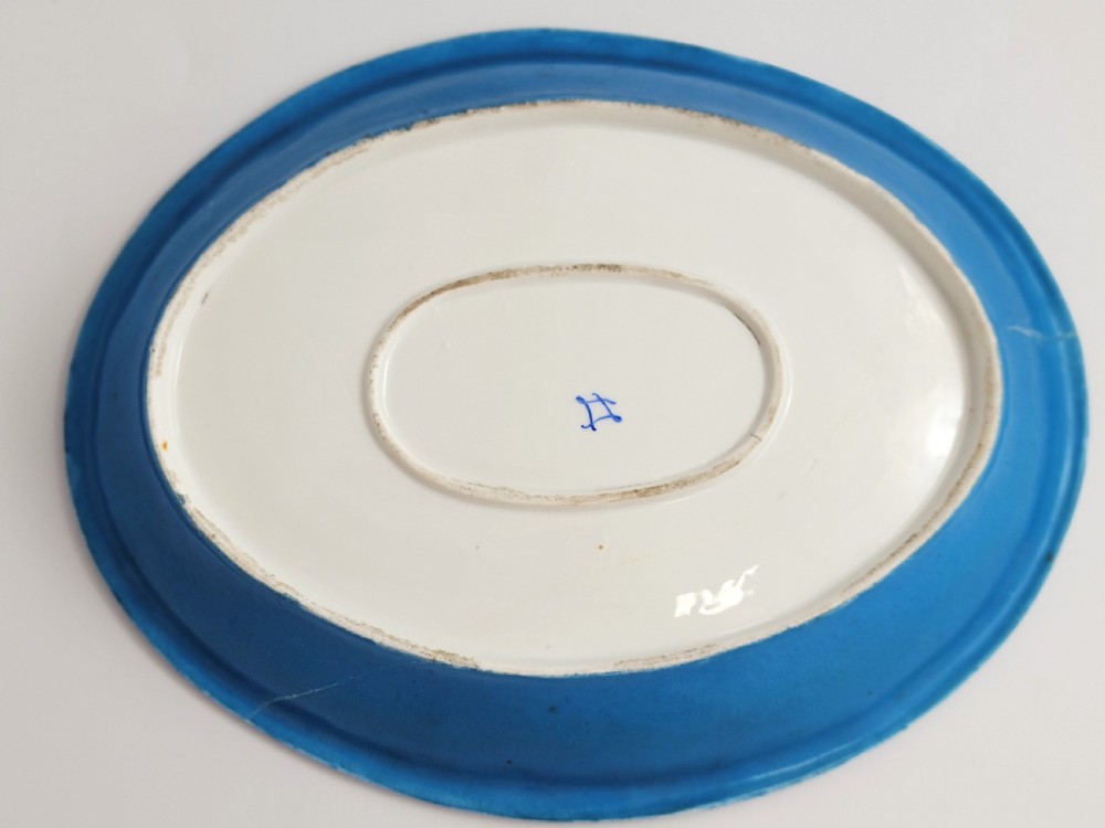An oval French porcelain tray featuring a bleu celeste ground with hand-painted floral reserves and a central scene depicting figures in a landscape enclosed by gilt ornamentation. View IV