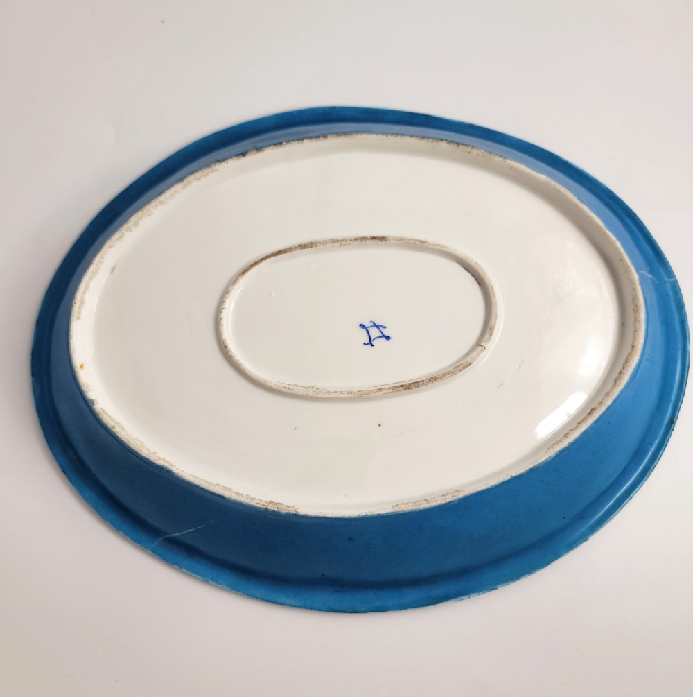 An oval French porcelain tray featuring a bleu celeste ground with hand-painted floral reserves and a central scene depicting figures in a landscape enclosed by gilt ornamentation. View V