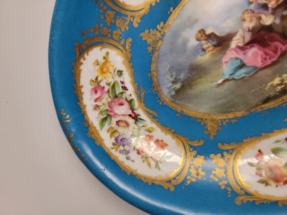 An oval French porcelain tray featuring a bleu celeste ground with hand-painted floral reserves and a central scene depicting figures in a landscape enclosed by gilt ornamentation. View IX