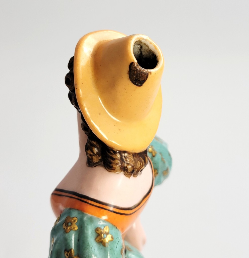 An early 19th-century French hard-paste porcelain figural scent bottle depicting a standing woman in a teal patterned dress, orange bodice, and yellow hat, mounted on a gilded shaped base. View IX