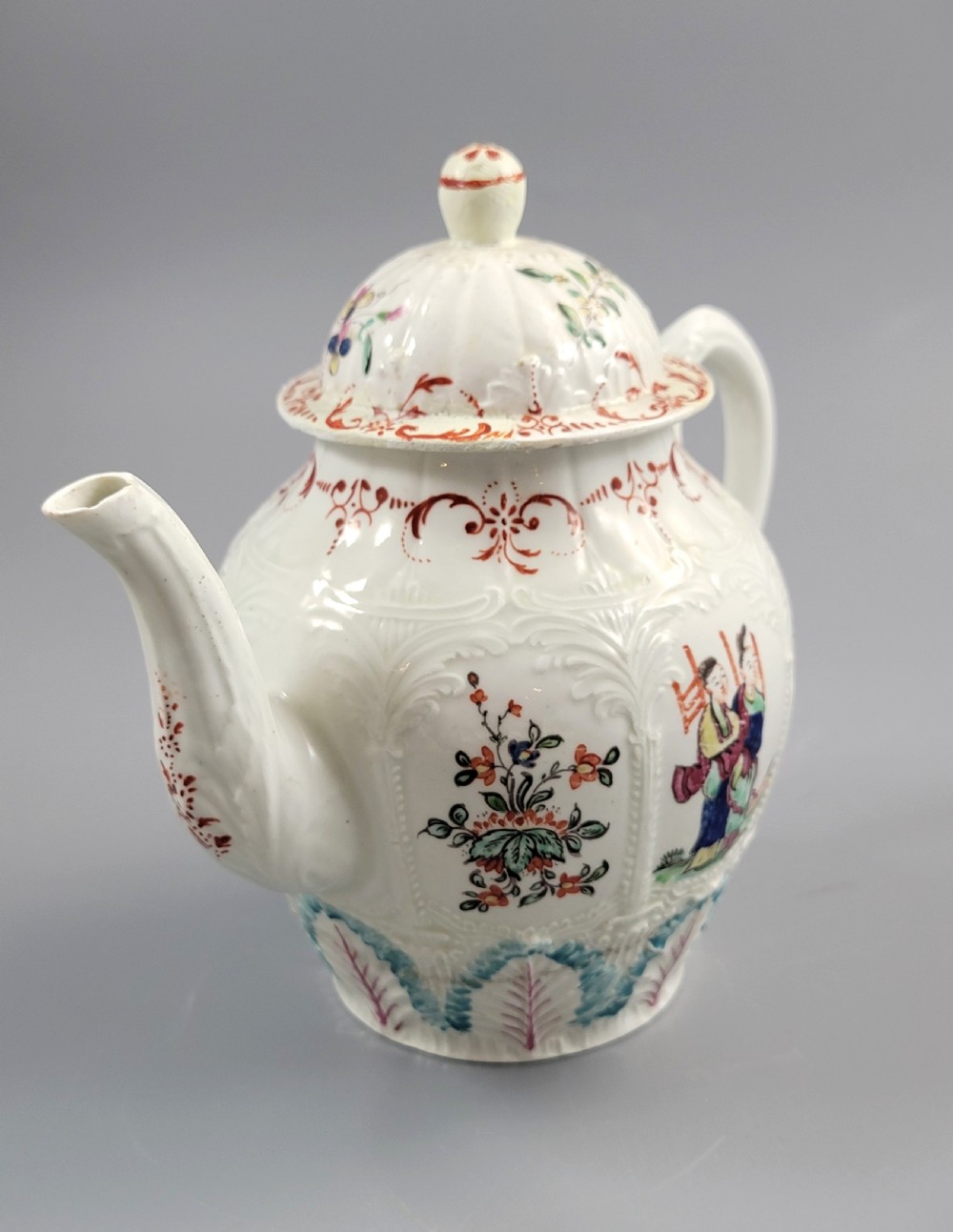A Georgian soft-paste porcelain teapot decorated with hand-painted Chinoiserie figures, floral sprays, and moulded leaf work around the base. View VI