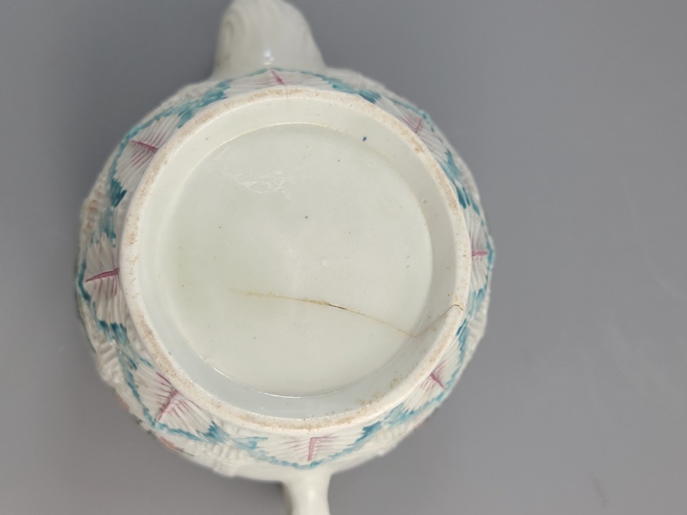 A Georgian soft-paste porcelain teapot decorated with hand-painted Chinoiserie figures, floral sprays, and moulded leaf work around the base. View XV