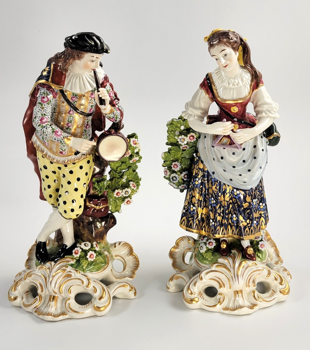 A pair of 19th-century French Samson porcelain figures depicting a male musician with a pipe and drum alongside a female musician holding a triangle, set on gilded rococo scrollwork bases.