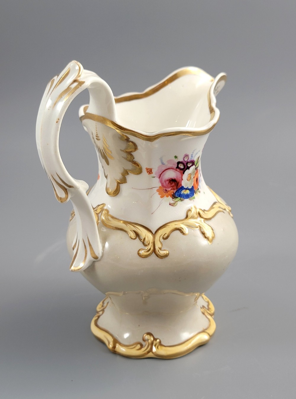 A white porcelain jug decorated with a hand-painted floral spray, gilded acanthus leaf scrollwork, a shaped spout, and a looped handle. View III