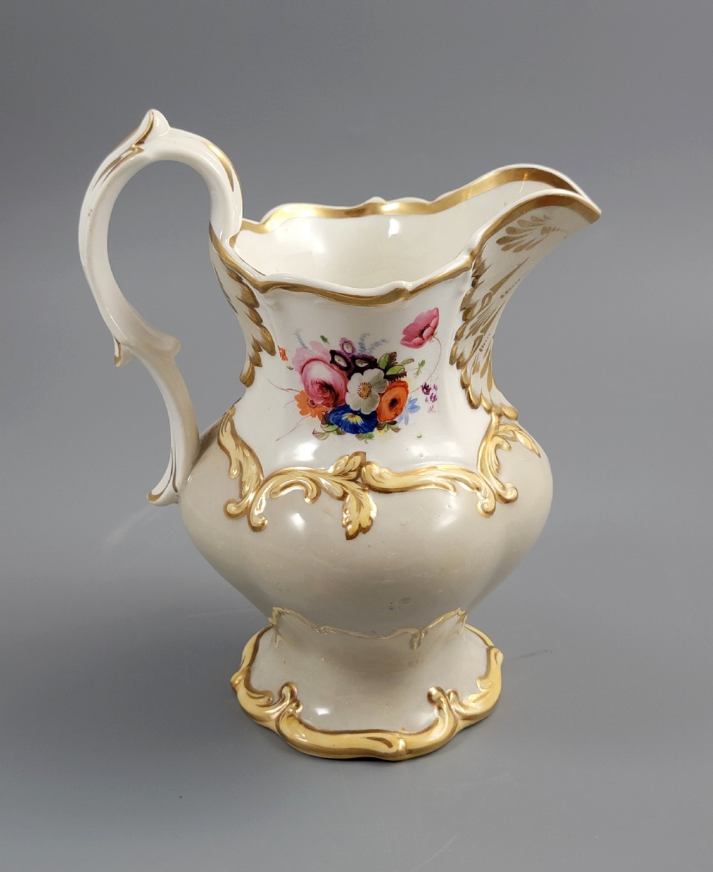 A white porcelain jug decorated with a hand-painted floral spray, gilded acanthus leaf scrollwork, a shaped spout, and a looped handle. View IV