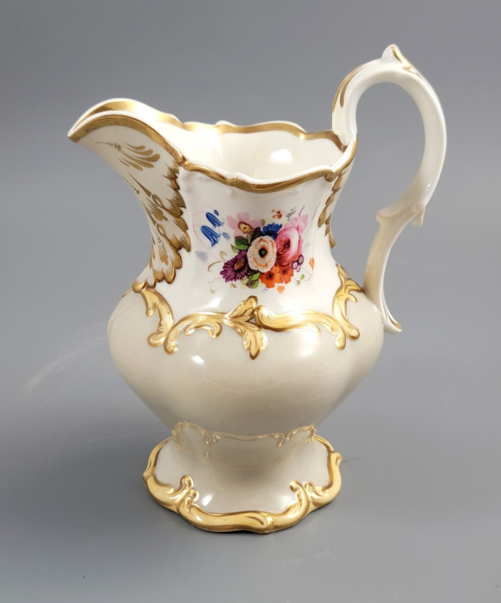 A white porcelain jug decorated with a hand-painted floral spray, gilded acanthus leaf scrollwork, a shaped spout, and a looped handle. View VII