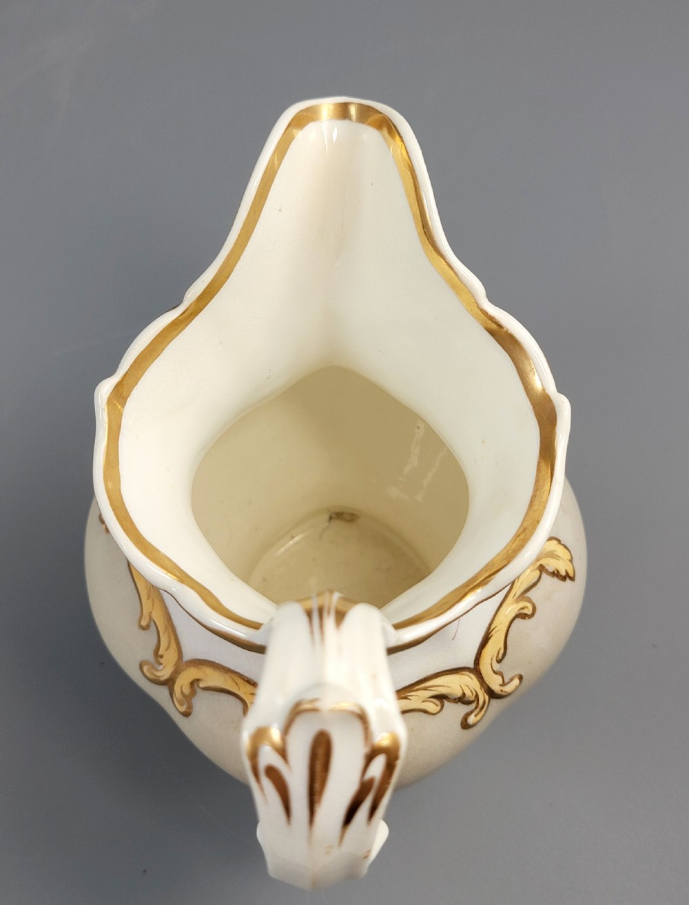 A white porcelain jug decorated with a hand-painted floral spray, gilded acanthus leaf scrollwork, a shaped spout, and a looped handle. View VIII