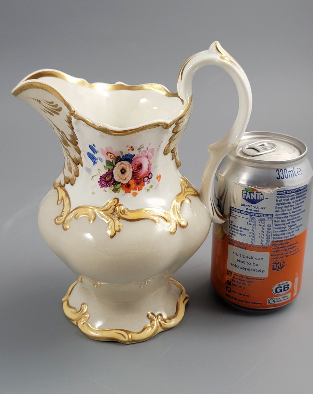 A white porcelain jug decorated with a hand-painted floral spray, gilded acanthus leaf scrollwork, a shaped spout, and a looped handle. View XI