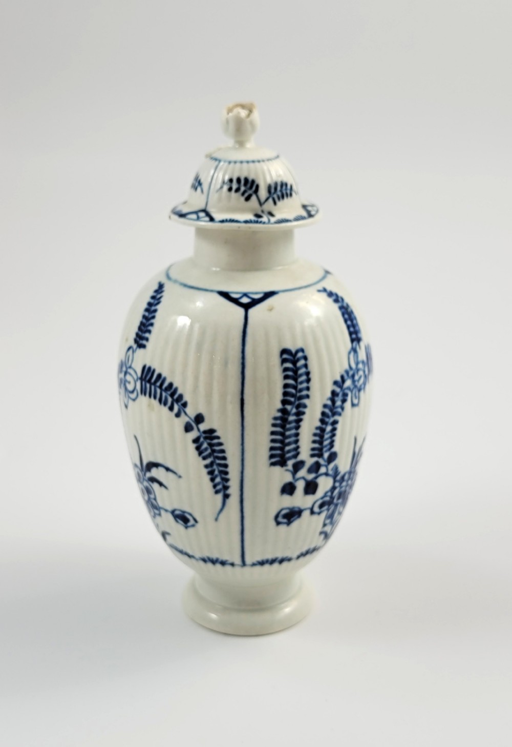 An eighteenth-century fluted soft-paste porcelain tea canister featuring underglaze blue floral patterns and a matching lid with a flower bud finial.