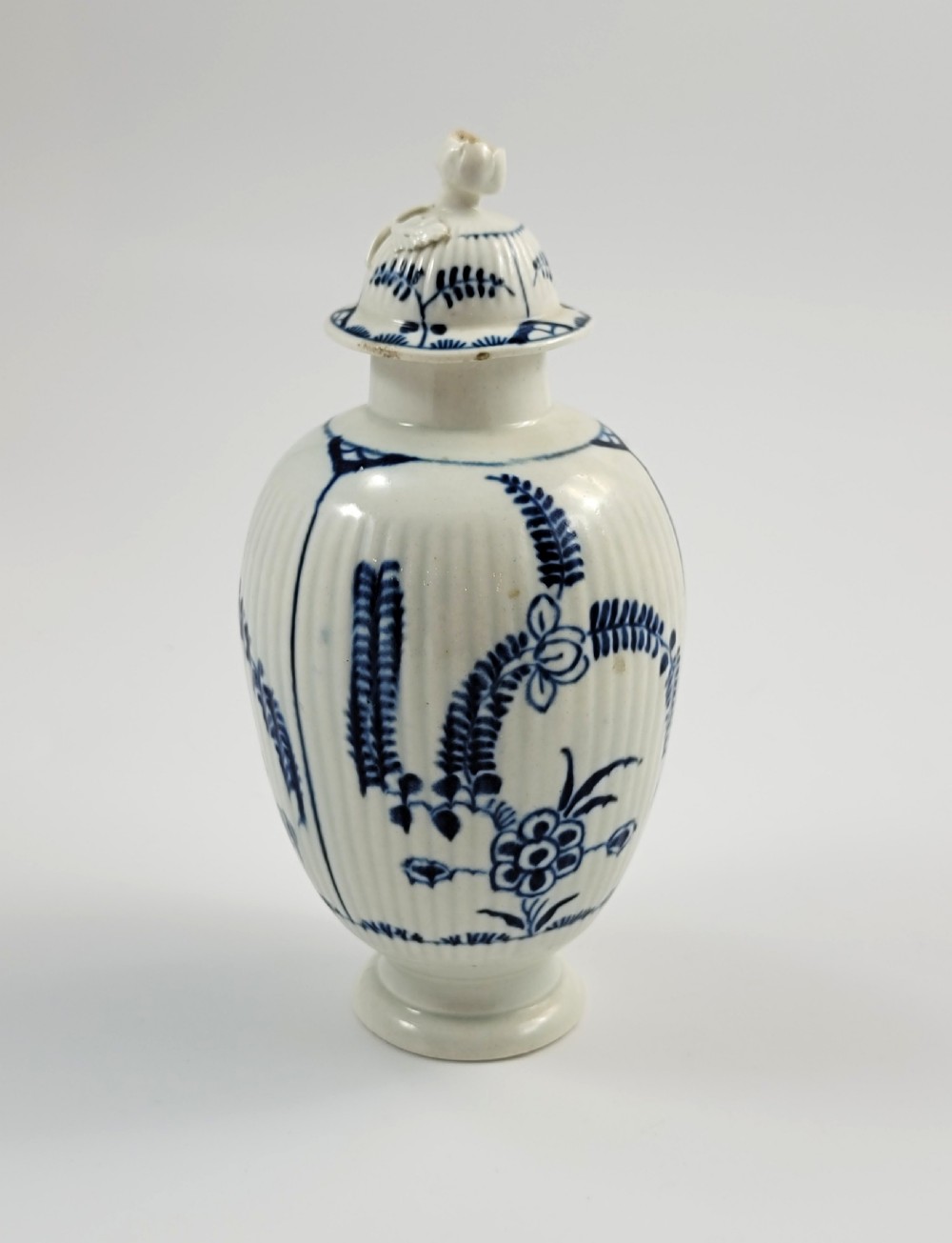 An eighteenth-century fluted soft-paste porcelain tea canister featuring underglaze blue floral patterns and a matching lid with a flower bud finial. View VI