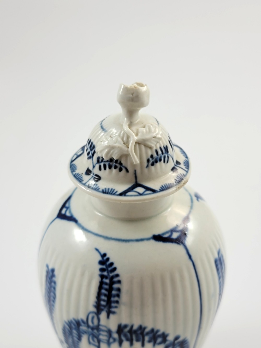 An eighteenth-century fluted soft-paste porcelain tea canister featuring underglaze blue floral patterns and a matching lid with a flower bud finial. View VII