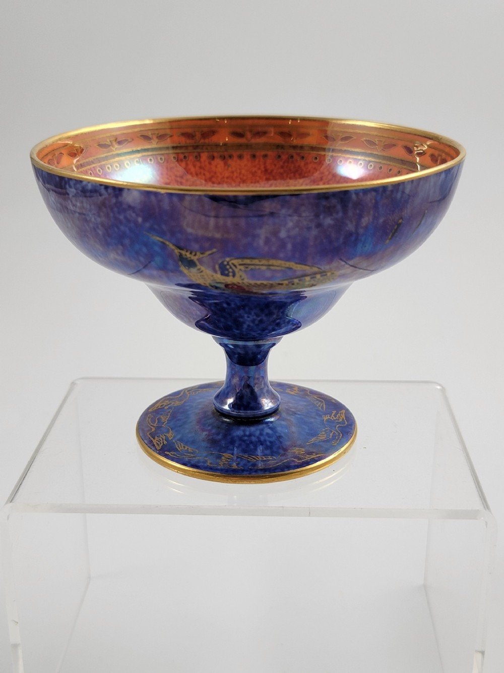 A footed porcelain melba cup featuring a mottled cobalt blue exterior with gilt hummingbird motifs and a bright orange iridescent interior finish.