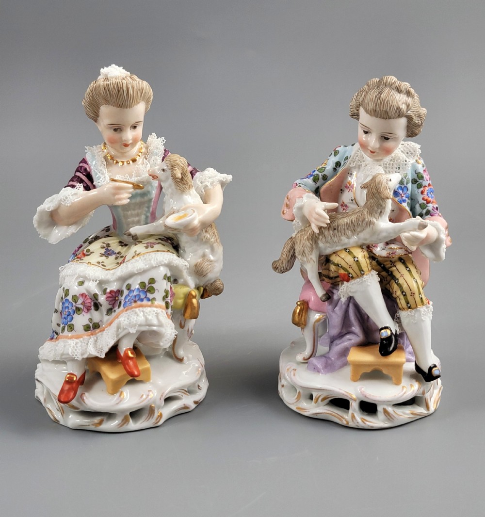 A pair of late 19th-century Sitzendorf porcelain figurines depicting a boy and girl in 18th-century clothing seated with pet lambs on gilded scrollwork bases.