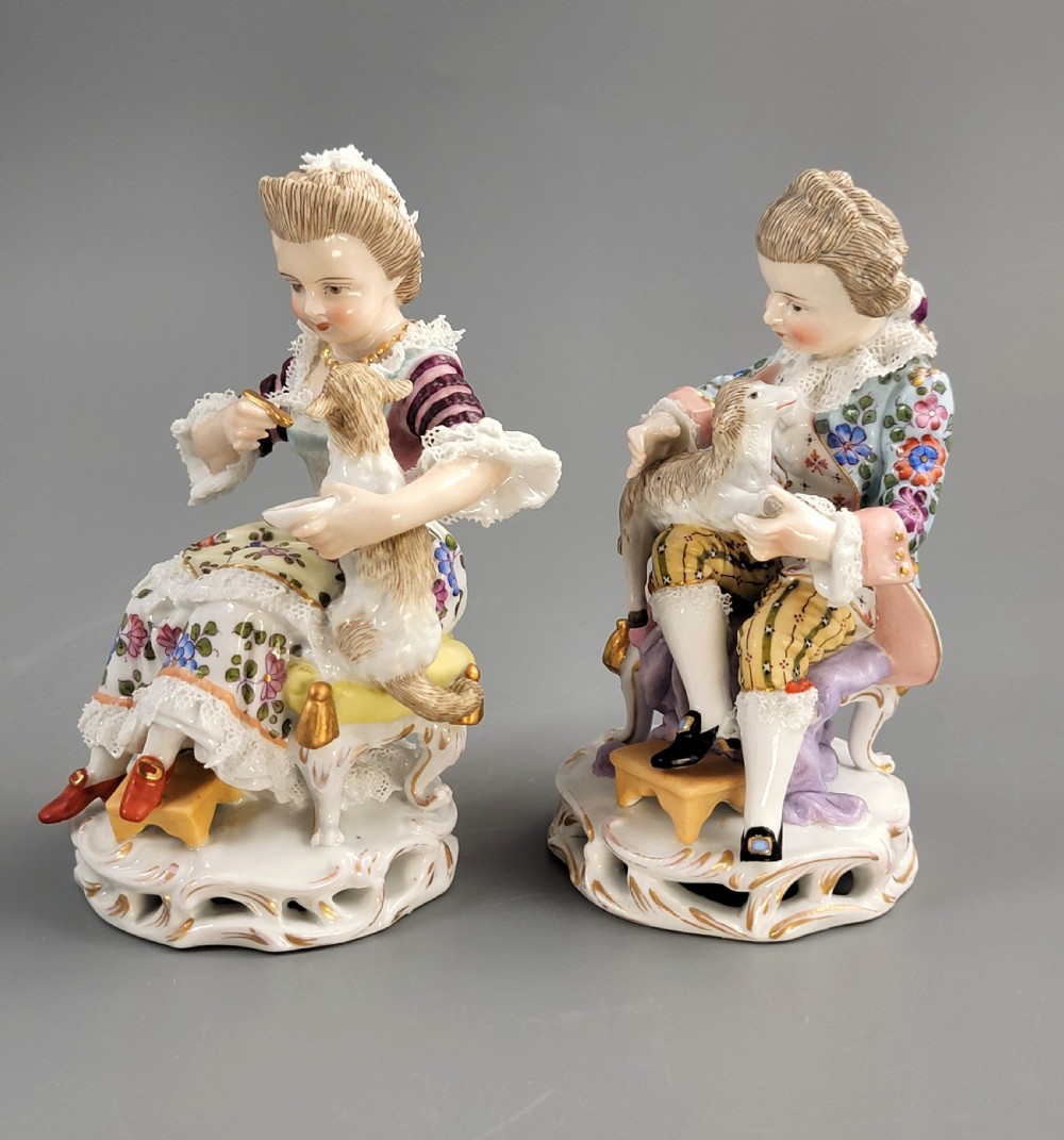 A pair of late 19th-century Sitzendorf porcelain figurines depicting a boy and girl in 18th-century clothing seated with pet lambs on gilded scrollwork bases. View II