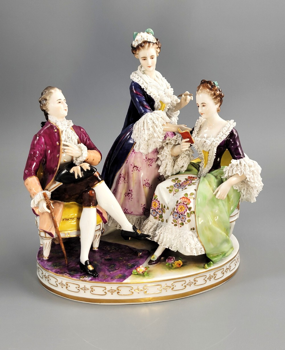 A German Volkstedt porcelain group depicting three eighteenth-century figures in elaborate attire seated on an oval gilt-decorated base.