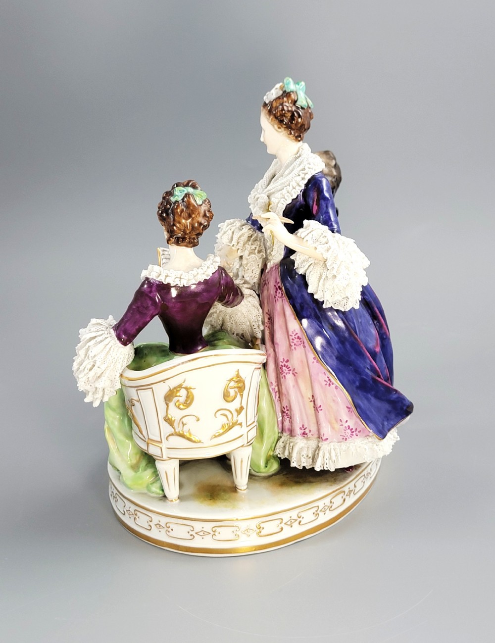 A German Volkstedt porcelain group depicting three eighteenth-century figures in elaborate attire seated on an oval gilt-decorated base. View III