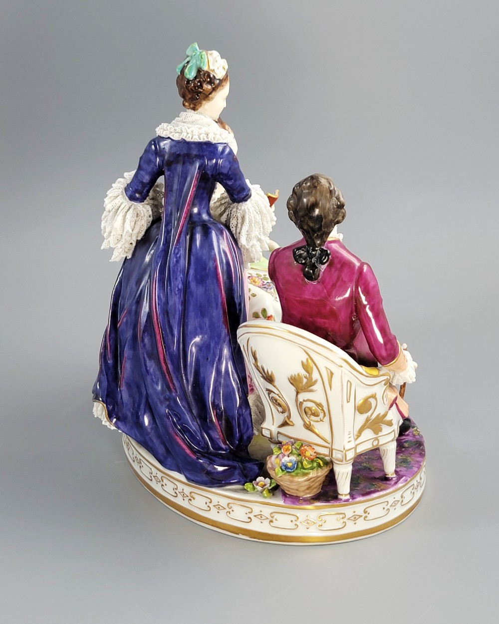 A German Volkstedt porcelain group depicting three eighteenth-century figures in elaborate attire seated on an oval gilt-decorated base. View IV