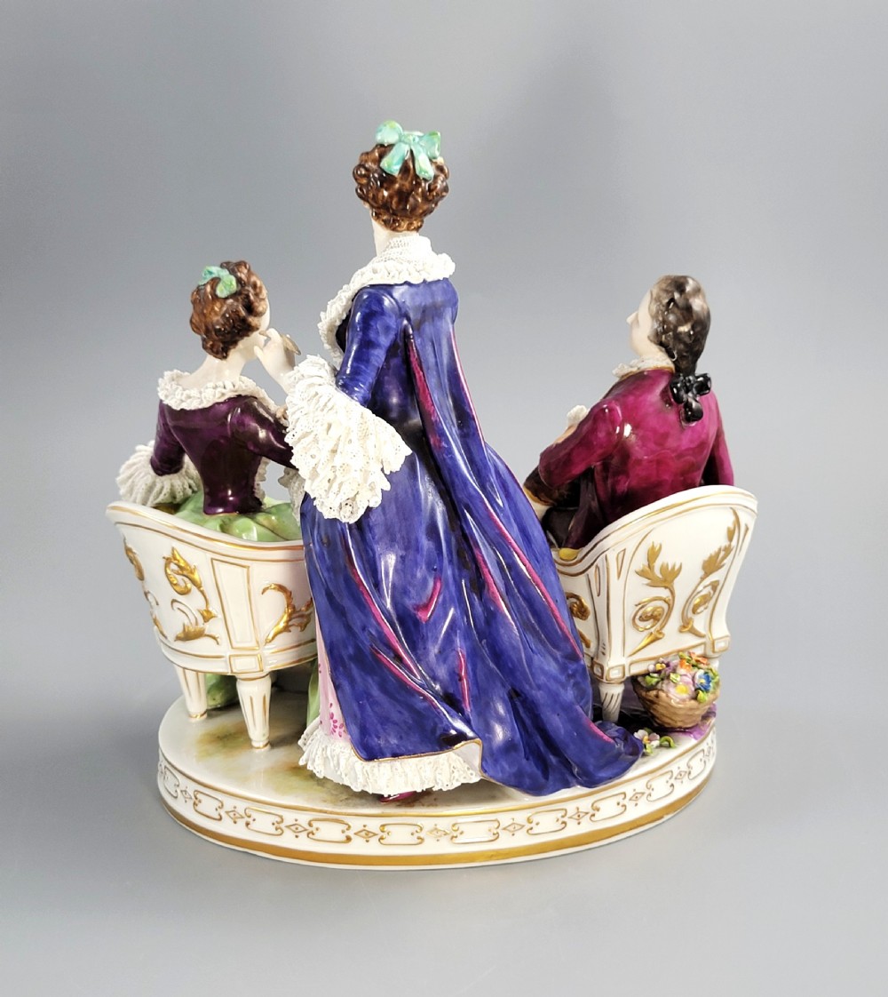 A German Volkstedt porcelain group depicting three eighteenth-century figures in elaborate attire seated on an oval gilt-decorated base. View VI