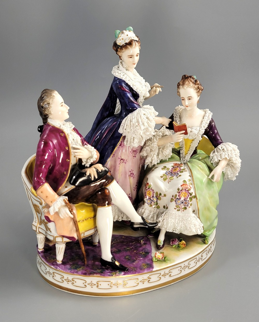 A German Volkstedt porcelain group depicting three eighteenth-century figures in elaborate attire seated on an oval gilt-decorated base. View VII