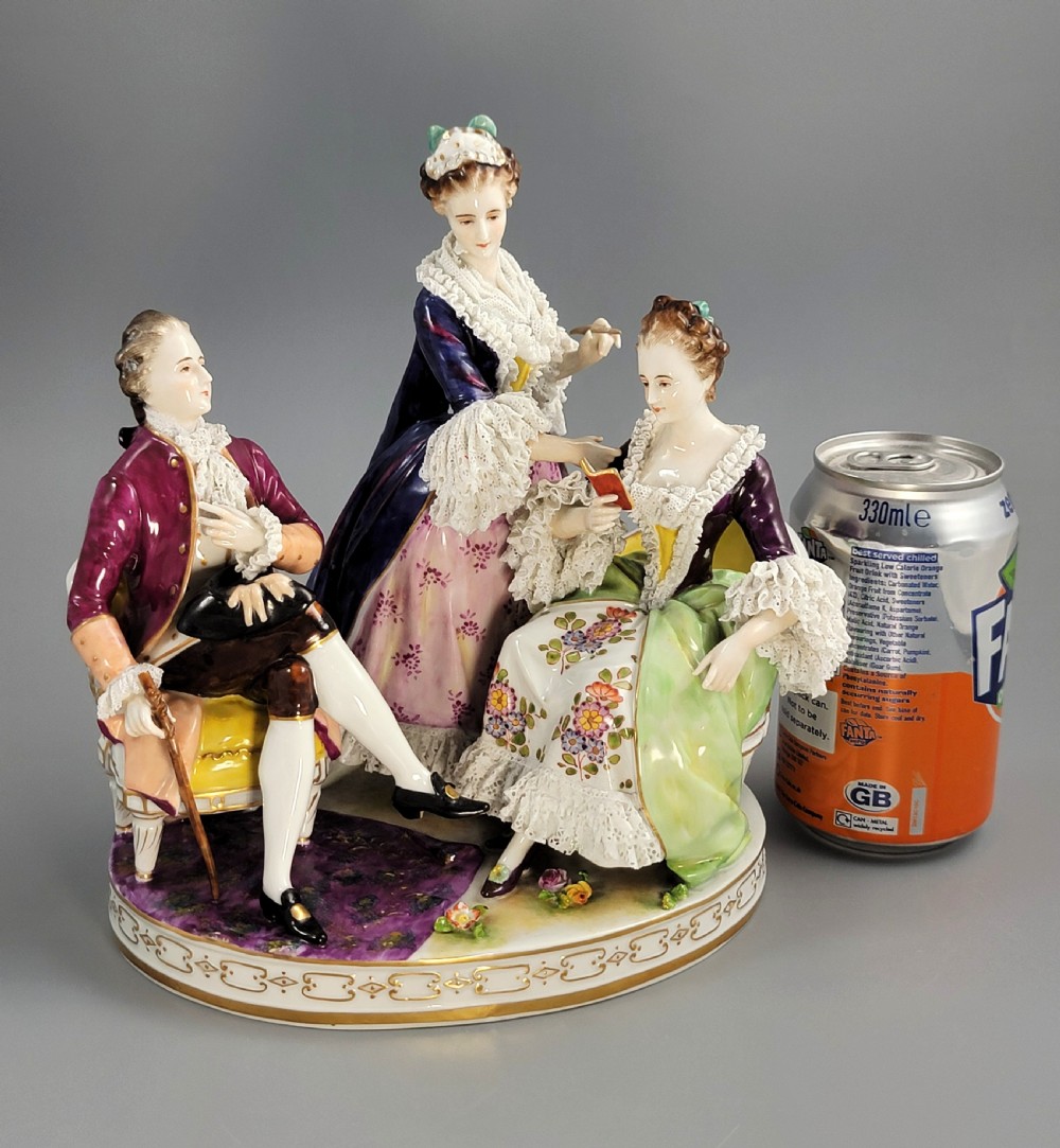 A German Volkstedt porcelain group depicting three eighteenth-century figures in elaborate attire seated on an oval gilt-decorated base. View IX