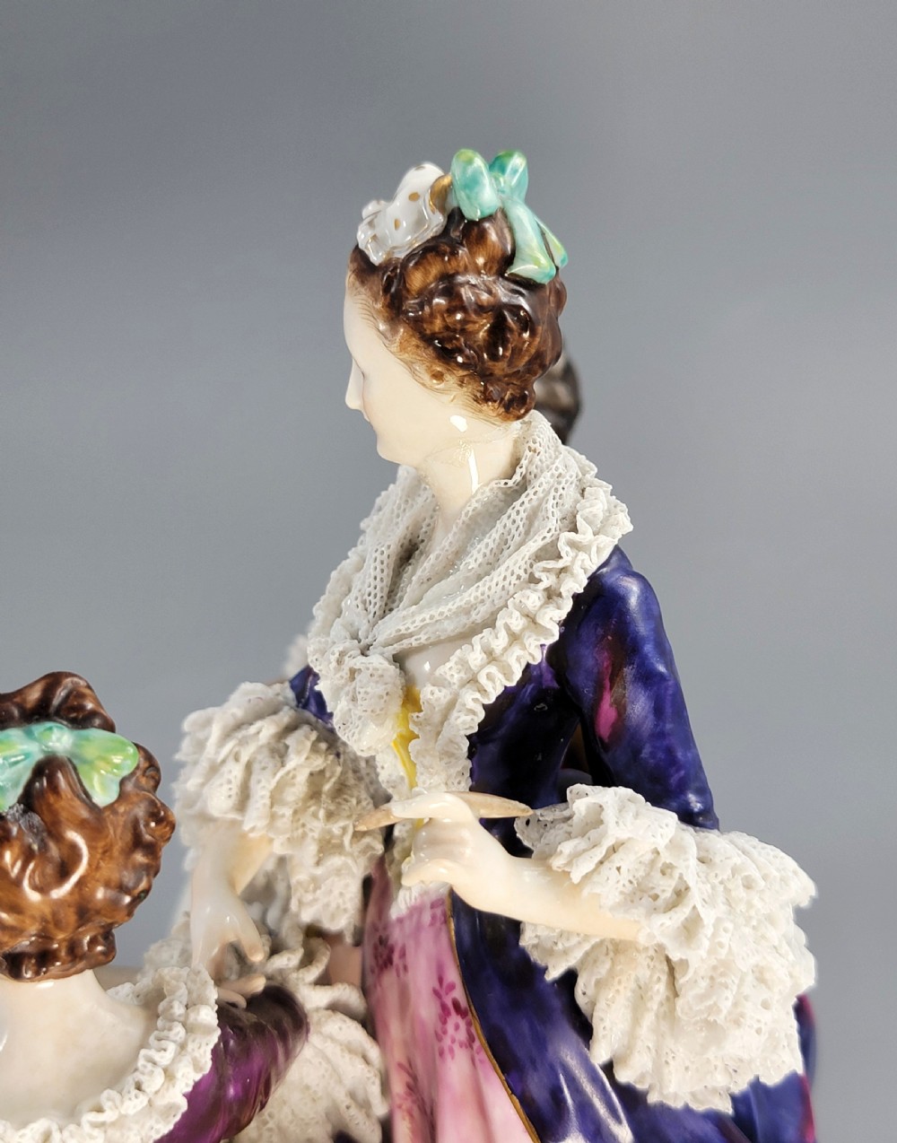 A German Volkstedt porcelain group depicting three eighteenth-century figures in elaborate attire seated on an oval gilt-decorated base. View XI