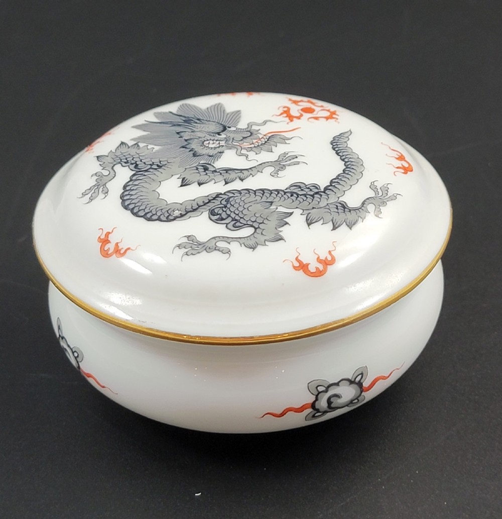 A circular white porcelain lidded trinket box adorned with a hand-painted grey dragon motif, red flame accents, and a gold gilt rim. View IV