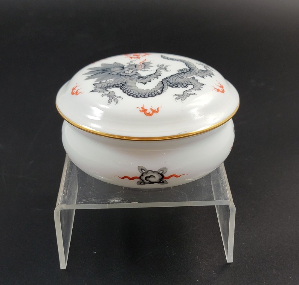 A circular white porcelain lidded trinket box adorned with a hand-painted grey dragon motif, red flame accents, and a gold gilt rim. View XII