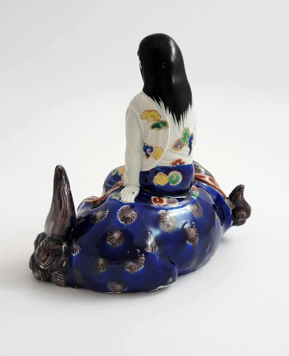 A Japanese Kutani porcelain figure depicting the deity Kannon seated atop a reclined blue shishi lion with detailed polychrome enamelled robes. View III