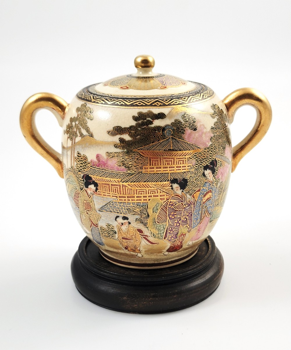 A lidded Japanese Satsuma ceramic sugar bowl with two gilt handles, crackle glaze, and hand-painted figures in a landscape.
