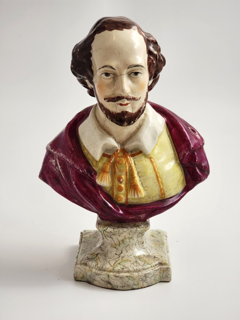 A painted ceramic portrait bust of William Shakespeare featuring a purple mantle, yellow doublet, and marbled base.