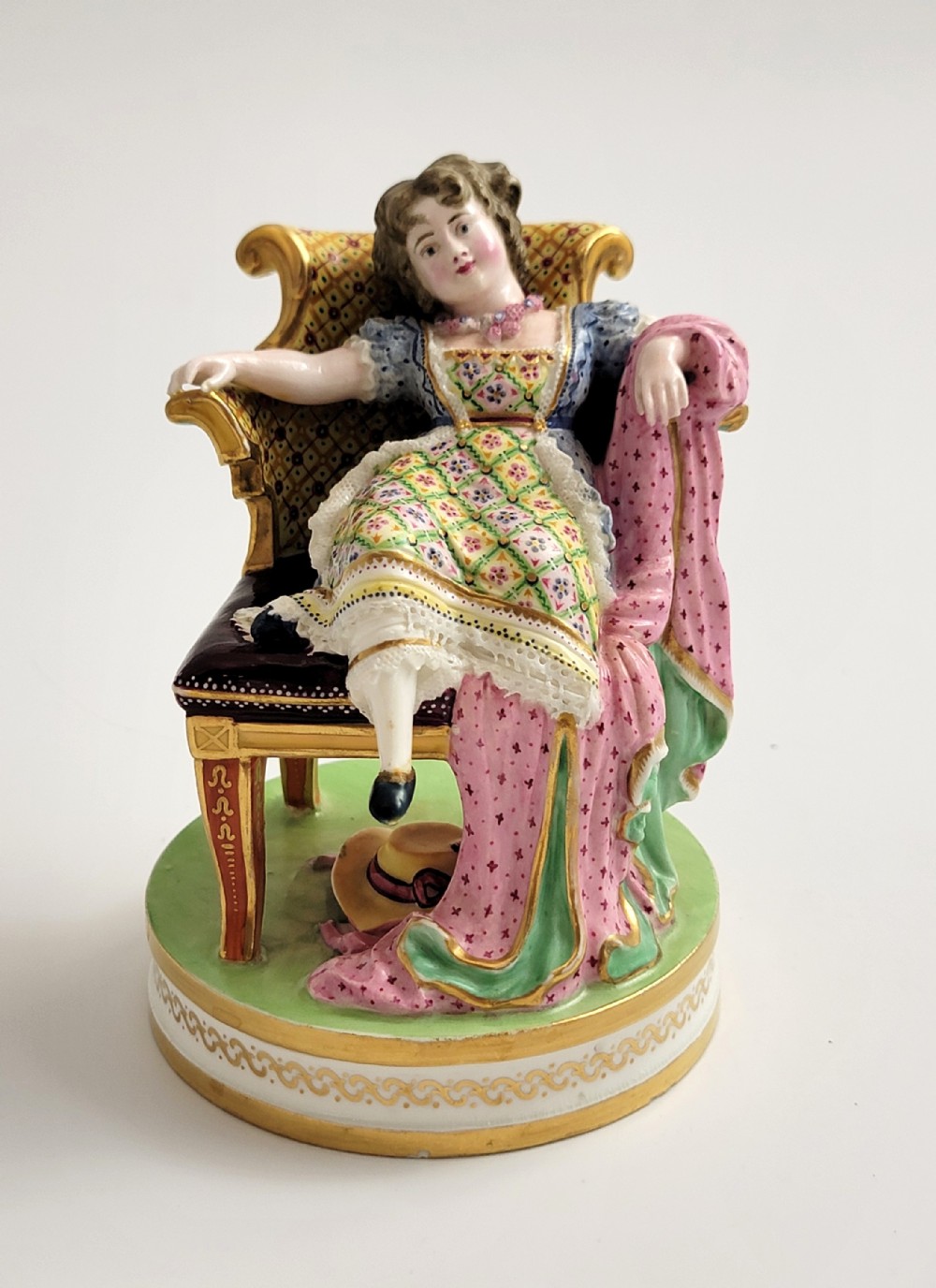 An 18th-century Derby soft-paste porcelain figurine depicting a seated woman in a colourful dress reclining on a gilded armchair.