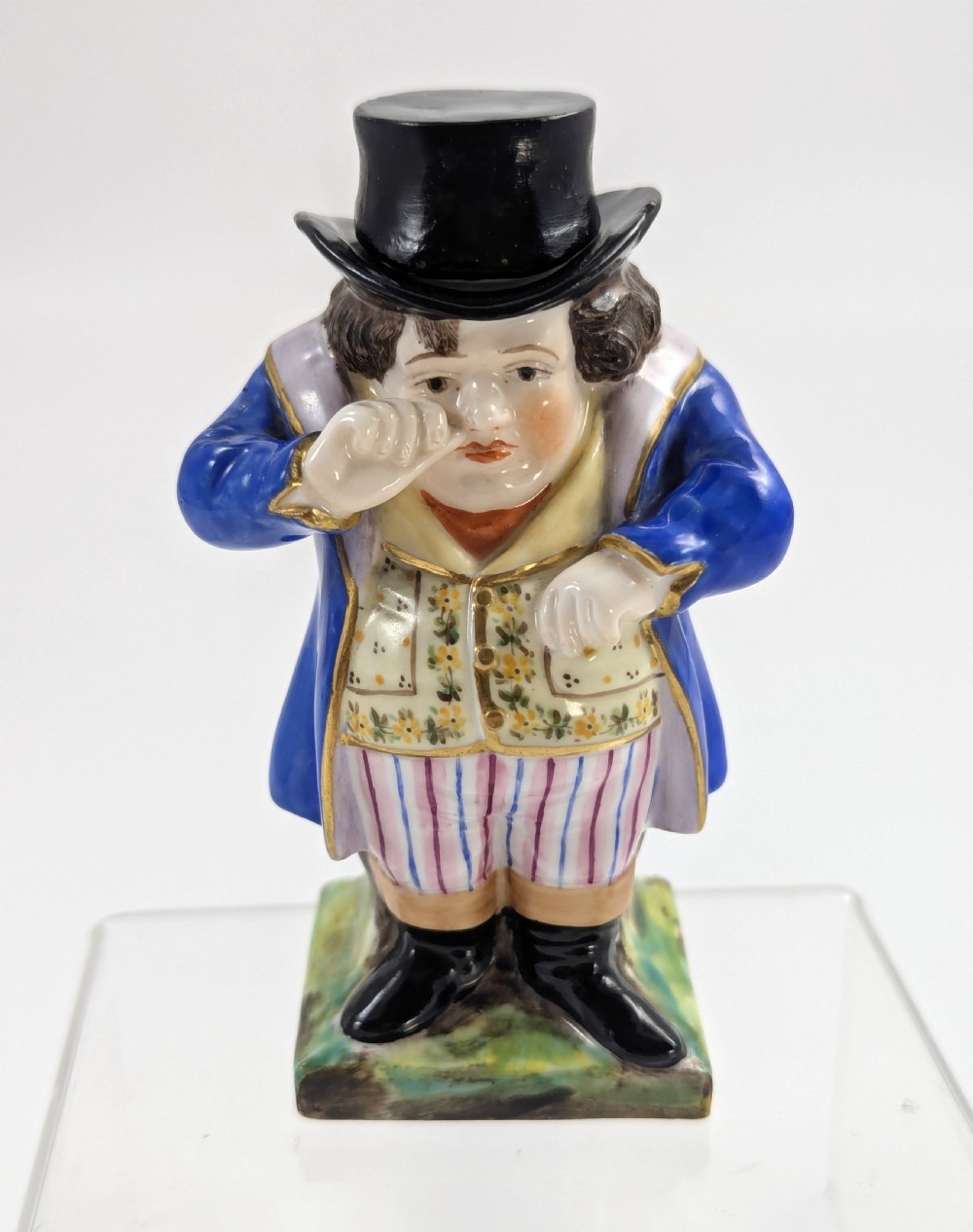 A porcelain Toby jug depicting a gentleman in a black top hat, blue coat, and striped trousers taking snuff.